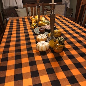 A Thanksgiving table setting with a black and orange checkered tablecloth. The table is set with black plates, gold chargers, and black wine glasses. There are also black and white skull decorations on the table.
