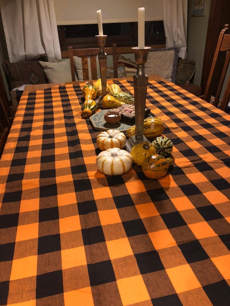 A Thanksgiving table setting with a black and orange checkered tablecloth. The table is set with black plates, gold chargers, and black wine glasses. There are also black and white skull decorations on the table.