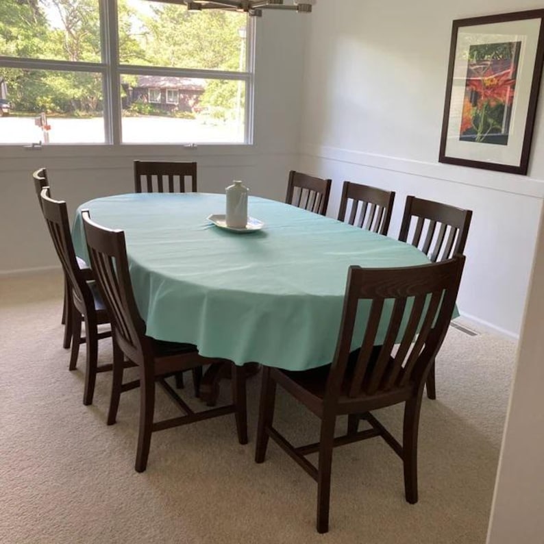 Mint green oval tablecloth on a wood table, wood chairs in a home dining room.