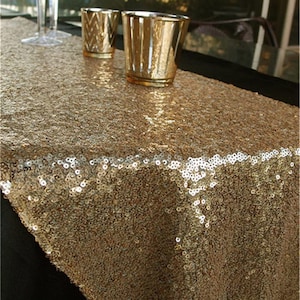 May include: Gold sequin table runner. The runner is made of a sparkly gold fabric and is perfect for adding a touch of glamour to any table setting.