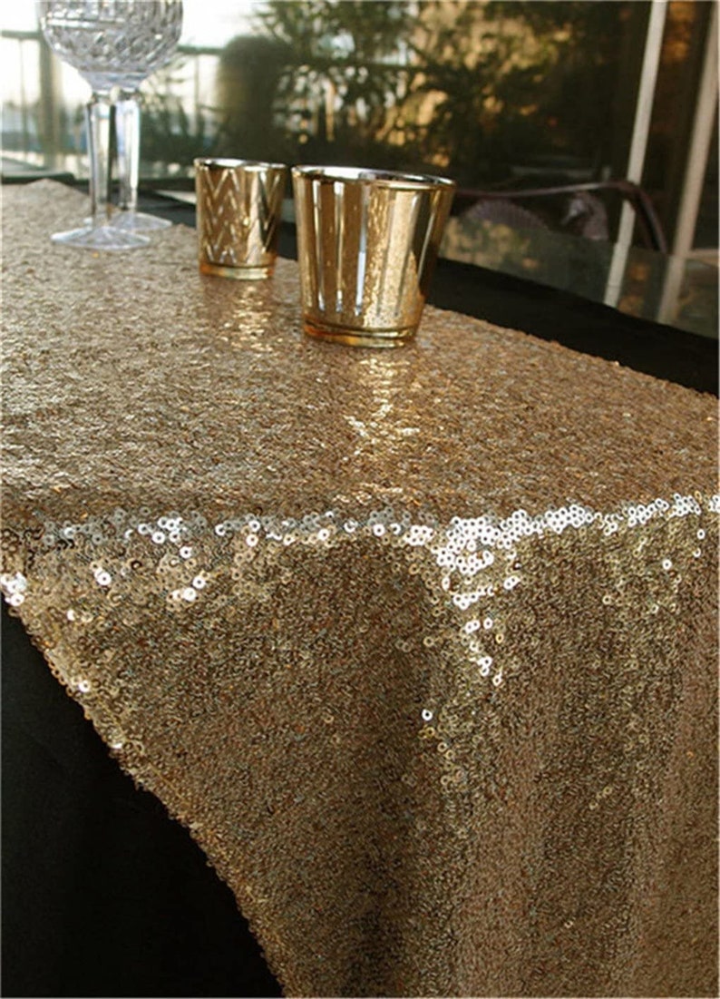May include: Gold sequin table runner. The runner is made of a sparkly gold fabric and is perfect for adding a touch of glamour to any table setting.