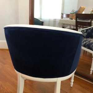 Puede incluir: Una silla con un respaldo tapizado en terciopelo azul marino profundo y una estructura de madera pintada de blanco. El respaldo curvo est&aacute; rematado con un borde blanco liso y la silla se apoya sobre cuatro patas delgadas de madera blanca.