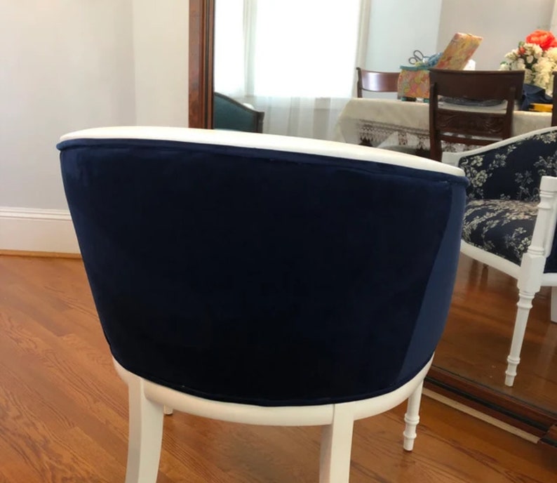 Puede incluir: Una silla con un respaldo tapizado en terciopelo azul marino profundo y una estructura de madera pintada de blanco. El respaldo curvo est&aacute; rematado con un borde blanco liso y la silla se apoya sobre cuatro patas delgadas de madera blanca.
