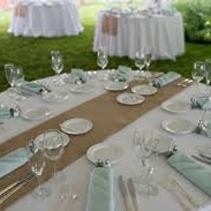 A round table set for a wedding reception with white linens, light blue napkins, and a burlap runner down the center.