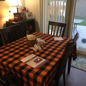 A black and orange plaid tablecloth is set on a table with four chairs. The tablecloth has a black and white pamphlet on top of it.
