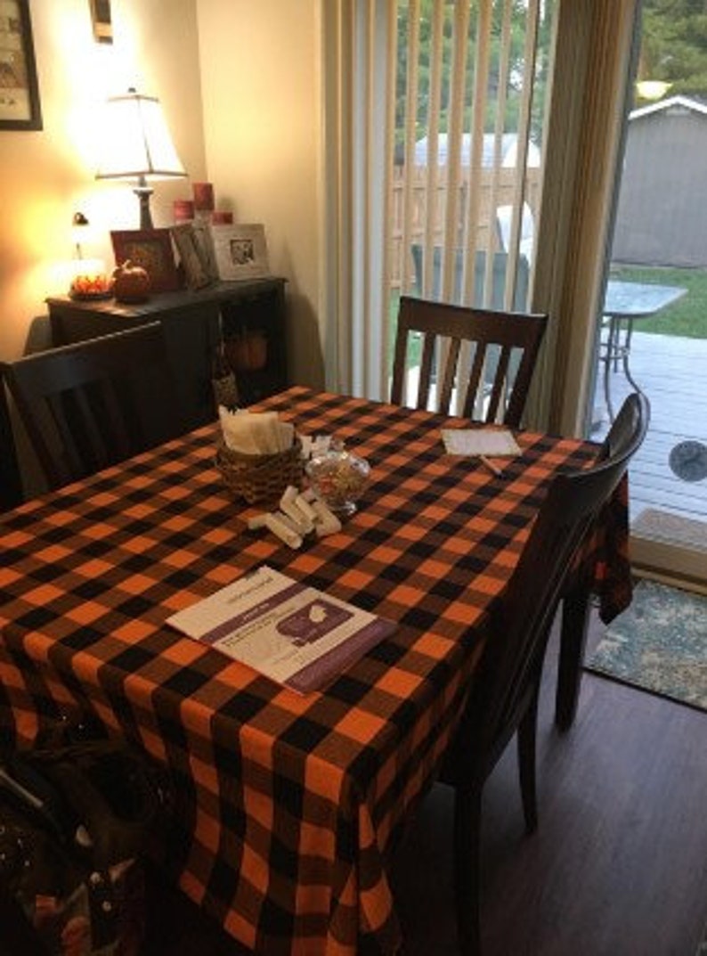 A black and orange plaid tablecloth is set on a table with four chairs. The tablecloth has a black and white pamphlet on top of it.