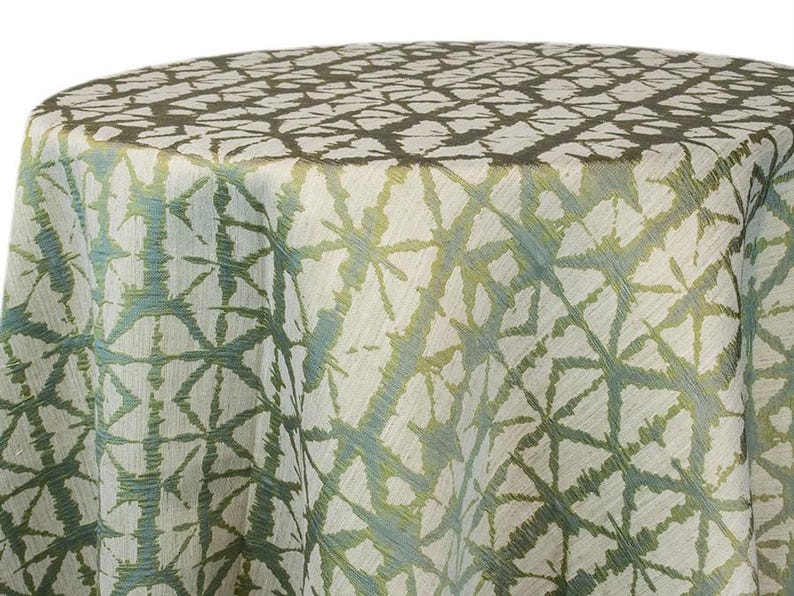 Moss green Shibori tablecloth with a geometric Shibori Hex pattern. The fabric has a textured appearance with a repeating diamond and line design. The tablecloth is draped over a round surface. The tablecloth manufacturer is Premier Linens.