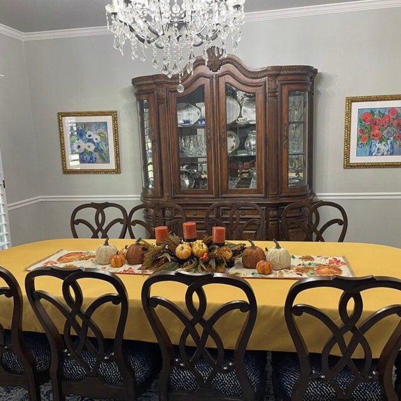 A large custom size oval table with a yellow tablecloth and a fall table runner with fall decorations on the table.