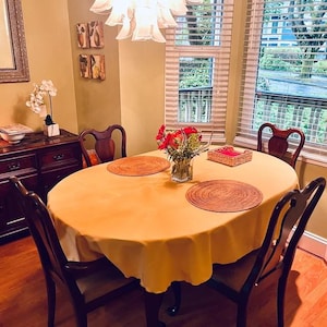 Gold table cloth and rod placemats on a small oval table with flower arrangement in someone's dining room.