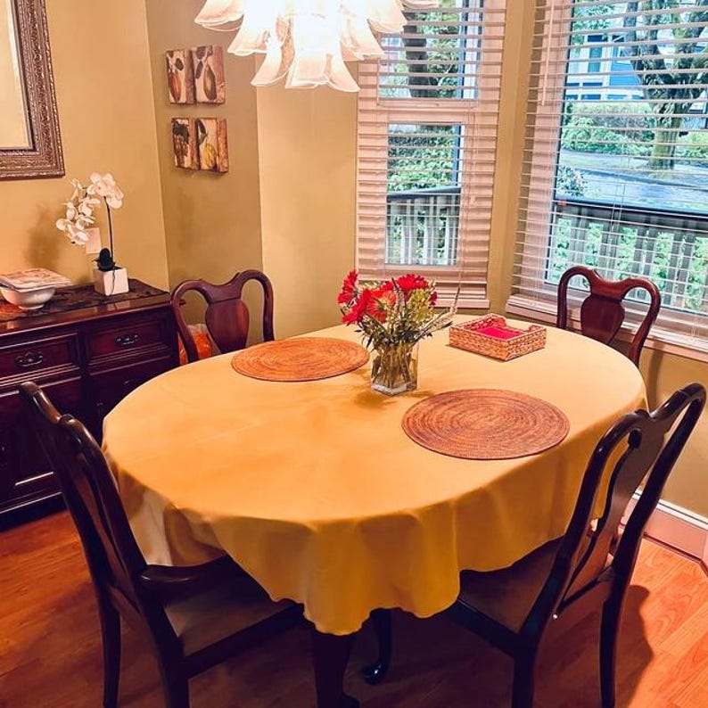 Gold table cloth and rod placemats on a small oval table with flower arrangement in someone's dining room.