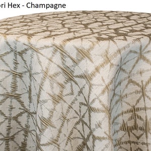Champagne Shibori tablecloth with a geometric Shibori Hex pattern. The fabric has a textured appearance with a repeating diamond and line design. The tablecloth is draped over a round surface. The tablecloth manufacturer is Premier Linens.