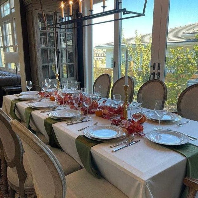 A white velvet tablecloth and a centerpiece of  flowers. The table is set with white plates, green velvet napkins, and clear glasses.