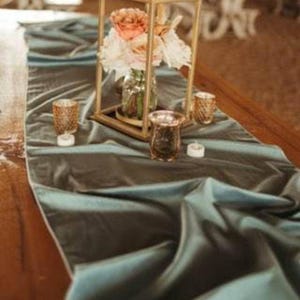 A green velvet table runner drapes over a wooden table set for a dinner party.
