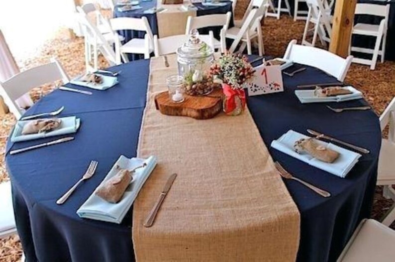 A wedding reception with blue tablecloths and burlap table runners. There are blue cloth napkins on the table.