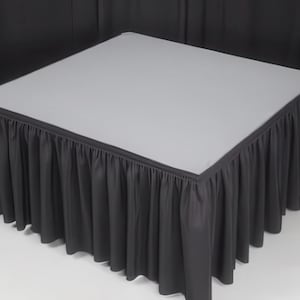 May include: A black table skirt with a white top. The skirt is pleated and has a smooth, flat surface.