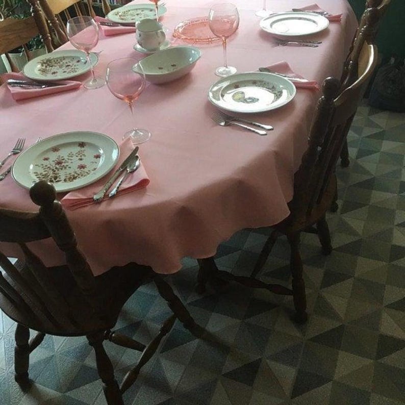 A pink oval tablecloth and napkins in the dining room of a home. China, silverware and glasses as the table is ready for an elegant meal.