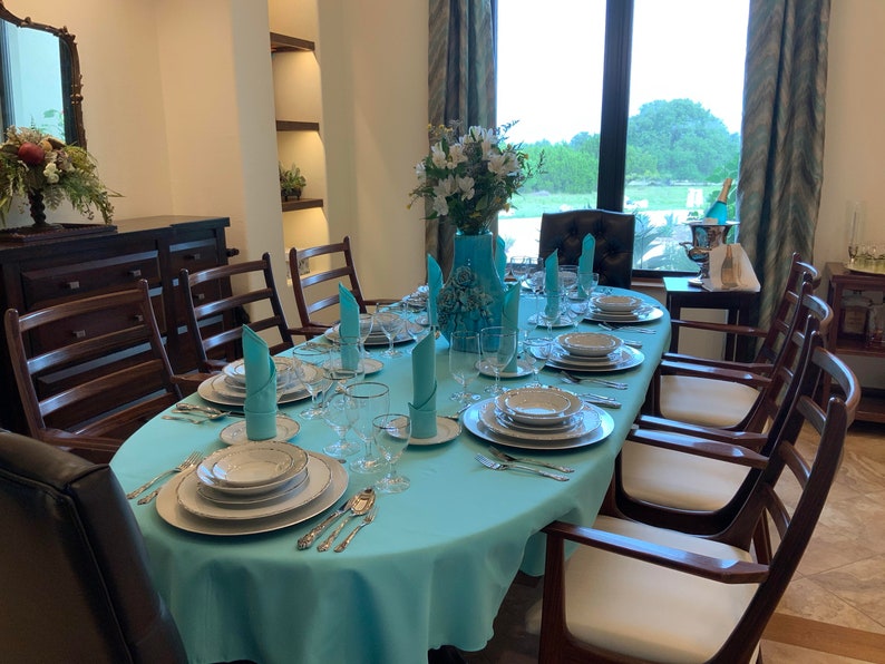 Beautiful turquoise oval tablecloth and folded napkins in a home dining room with an amazing view.