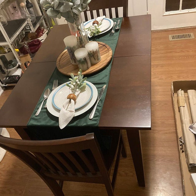May include: A dark wood dining table with two chairs, set for a holiday dinner. The table is decorated with a green tablecloth, white plates, and candles.