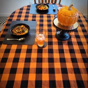 A black and orange checker tablecloth with two bowls of food and a glass of juice on top. A pumpkin sits on a cake stand in the center of the table.