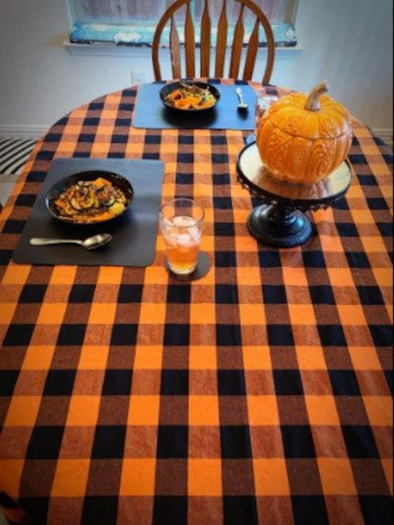 A black and orange checker tablecloth with two bowls of food and a glass of juice on top. A pumpkin sits on a cake stand in the center of the table.