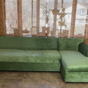 A green sectional sofa with a chaise lounge made with upholstery velvet. The sofa is covered in a soft, plush fabric.