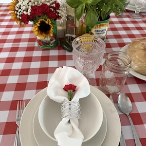 A table with a checkered red and white tablecloth and a napkin on top of the china with a red flower in the dinner napkin.