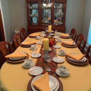 A yellow oval tablecloth, dinner napkins and red table runner in the dining room of a home. China, silverware and glasses as the table is ready for an elegant meal.