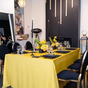 A yellow velvet tablecloth with black candlesticks and a centerpiece of yellow flowers. The table is set with black plates, black velvet napkins, and clear glasses. There are two black chairs with gold accents in the foreground.