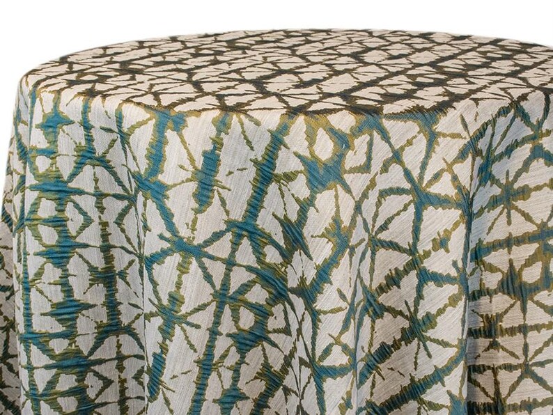 Emerald Shibori tablecloth with a geometric Shibori Hex pattern. The fabric has a textured appearance with a repeating diamond and line design. The tablecloth is draped over a round surface. The tablecloth manufacturer is Premier Linens.
