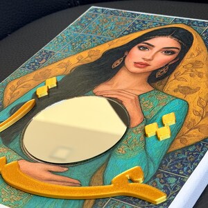 May include: A rectangular wall art piece featuring a portrait of a person with long dark hair wearing a teal garment and a gold head covering. A circular mirror is embedded in the center, surrounded by raised gold-colored geometric accents.