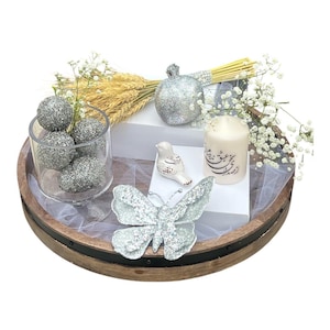 May include: A silver glitter butterfly, a silver glitter pomegranate, a white candle with calligraphy, and silver glitter balls in a glass vase are arranged on a wooden tray with a white sheer fabric overlay.