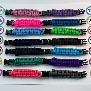 Puede incluir: Una fila de 13 pulseras de paracord de colores con hebillas de pl&aacute;stico negras. Las pulseras est&aacute;n numeradas del 15 al 28.