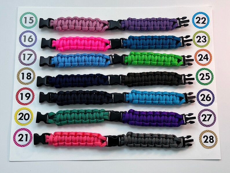 Puede incluir: Una fila de 13 pulseras de paracord de colores con hebillas de pl&aacute;stico negras. Las pulseras est&aacute;n numeradas del 15 al 28.