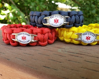 May include: Three paracord bracelets in red, navy blue, and yellow. Each bracelet features a central silver-toned oval charm with a white background, a red medical star symbol, and the black text "HAD A LIVER TRANSPLANT" printed on the surface.