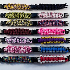 Puede incluir: Diez pulseras de paracord de colores con cierres de pl&aacute;stico negro. Las pulseras est&aacute;n dispuestas en una fila de arriba a abajo, etiquetadas de la A a la G a la izquierda y de la H a la M a la derecha.