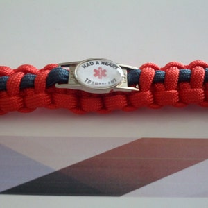 Puede incluir: Pulsera de paracord roja y negra con un dije de metal plateado que dice "Had a Heart" y presenta un s&iacute;mbolo de estrella de la vida roja.