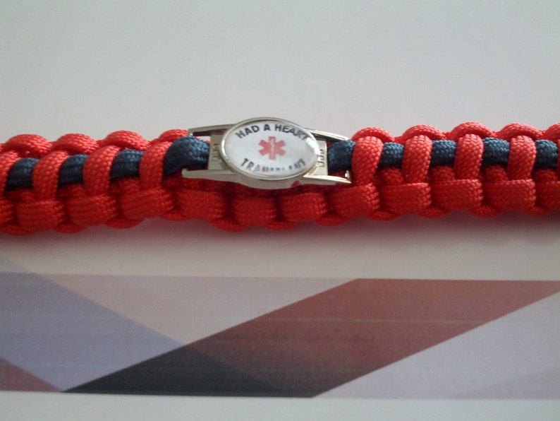 Puede incluir: Pulsera de paracord roja y negra con un dije de metal plateado que dice "Had a Heart" y presenta un s&iacute;mbolo de estrella de la vida roja.
