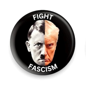 Puede incluir: Un botón negro con una imagen dividida de dos caras, una en blanco y negro y la otra en color. El lado en blanco y negro tiene un bigote. El texto "FIGHT" está en la parte superior y "FASCISM" en la inferior.