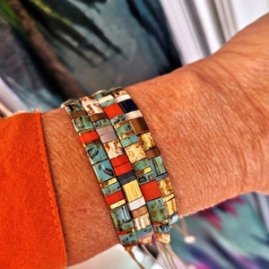 Op de afbeelding: Een set van vier kleurrijke kralenarmbanden met een turquoise, goud, rood, wit en zwart kleurenschema. De armbanden zijn gestapeld op de pols van een persoon.
