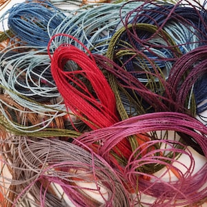 May include: A collection of embroidery floss spools in various colors, including red, blue, green, brown, and purple. The spools are tangled together, creating a colorful and textured image.