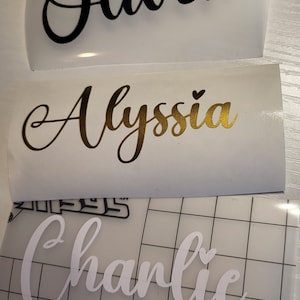 May include: Three white vinyl sheets with names written in black, gold, and white cursive lettering. The names are "Oliver", "Alyssa", and "Charlie".