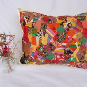 Könnte beinhalten: Ein rechteckiges Zierkissen mit einem lebendigen Patchwork-Design aus verschiedenen Stoffresten in Rot-, Orange-, Gelb-, Grün- und Violetttönen, das mit einer einfarbigen gelben Bordüre entlang der Kanten des Kissenbezugs versehen ist.