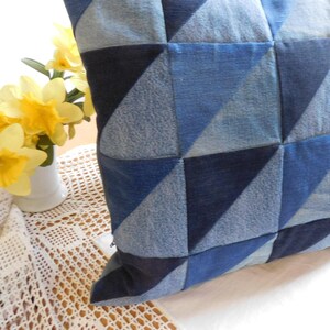 Könnte beinhalten: Quadratisches Denim-Kissen mit geometrischem Patchwork-Design in Blautönen. Der Denim hat verschiedene Waschungen, wodurch eine strukturierte Oberfläche entsteht. Ein dekoratives Wohnaccessoire.