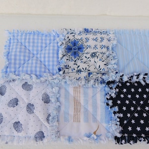 Könnte beinhalten: Ein Patchwork-Quilt mit verschiedenen blau-weißen Mustern. Designs umfassen Vichy, Blumen, Streifen, Muscheln und Sterne. Die Kanten sind mit einem Fransenbesatz versehen. Das Design deutet auf ein maritimes Thema hin.
