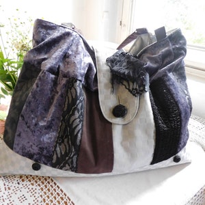 Könnte beinhalten: Eine weiße, braune und violette Patchwork-Tragetasche mit schwarzen Spitzenapplikationen und einem großen Knopf. Die Tasche hat ein gerafftes, gerüschtes Design.