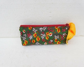 May include: A rectangular pencil case with a floral pattern. The case is primarily dark green with a repeating pattern of yellow, red, and white flowers. It has a red zipper and a yellow fabric accent.