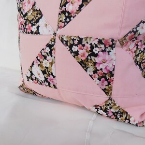 May include: A square throw pillow featuring a patchwork design of solid light pink fabric triangles alternating with black fabric triangles printed with a floral pattern of pink, white, and tan flowers and green leaves, stitched together with visible seams.