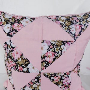 May include: A square throw pillow featuring a patchwork design of solid light pink fabric triangles alternating with black fabric triangles printed with a floral pattern of pink, white, and green flowers. The pillow has a visible seam construction.