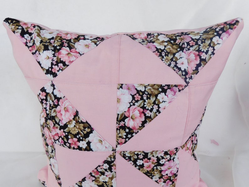 May include: A square throw pillow featuring a patchwork design of solid light pink fabric triangles alternating with black fabric triangles printed with a floral pattern of pink, white, and green flowers. The pillow has a visible seam construction.