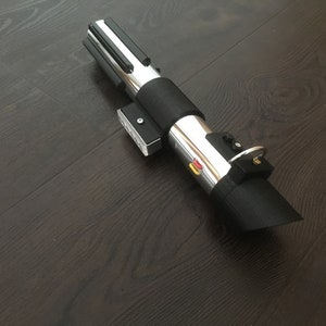 Pu&ograve; includere: Un accessorio per spada laser nero e argento con un'impugnatura nera e una lama argentata. L'impugnatura ha un pulsante nero e un anello argentato.